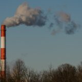 Smoke billows from a striped industrial chimney against blue sky.
